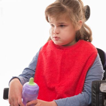 Girl sat in wheelchair wearing red cotton towelling apron.