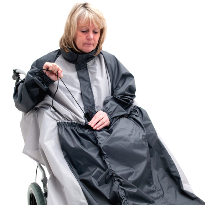 Woman wearing Black Grey wheelchair coat, pulling drawstring on coat.