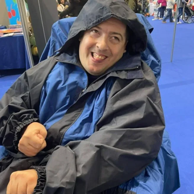 Man sin wheelchair smiling wearing a blue wheelchair coat