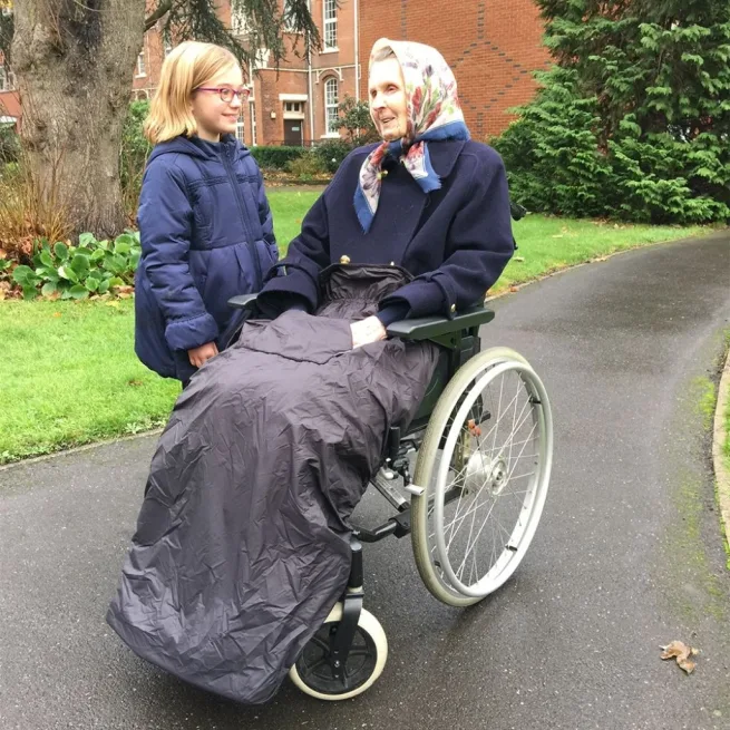 Woman in wheelchair with black cosy looking at young girl by her side