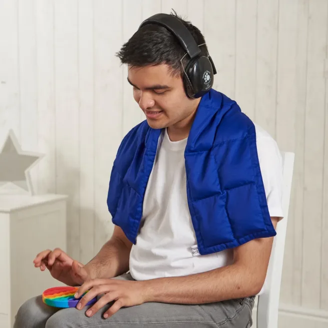 Boy sat in chair wearing blue weighted shoulder wrap around his shoulders