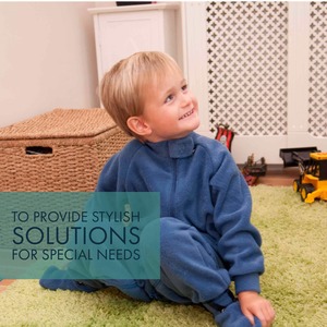 Boy sat on the floor wearing blue front opening sleepsuit designed for children with special needs.