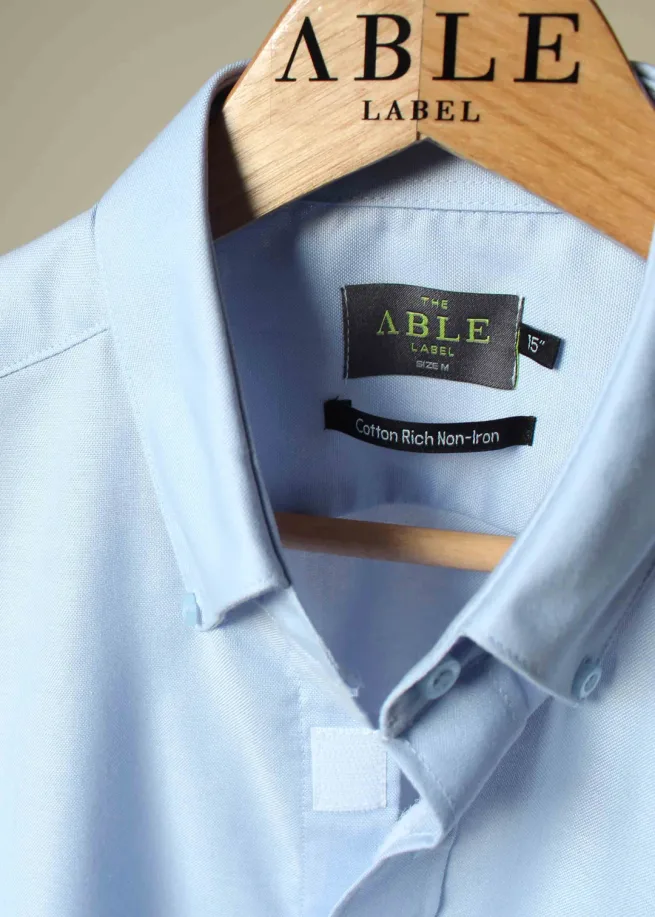 Close up of oxford blue shirt on hanger showing the neckline and velcro fastening.